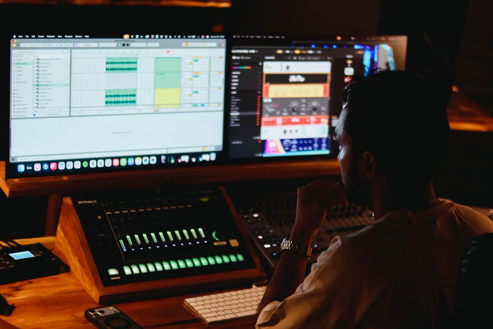 Producer at a studio desk at night, Ableton and a plugin on two screens, Roland drum machine in front of him