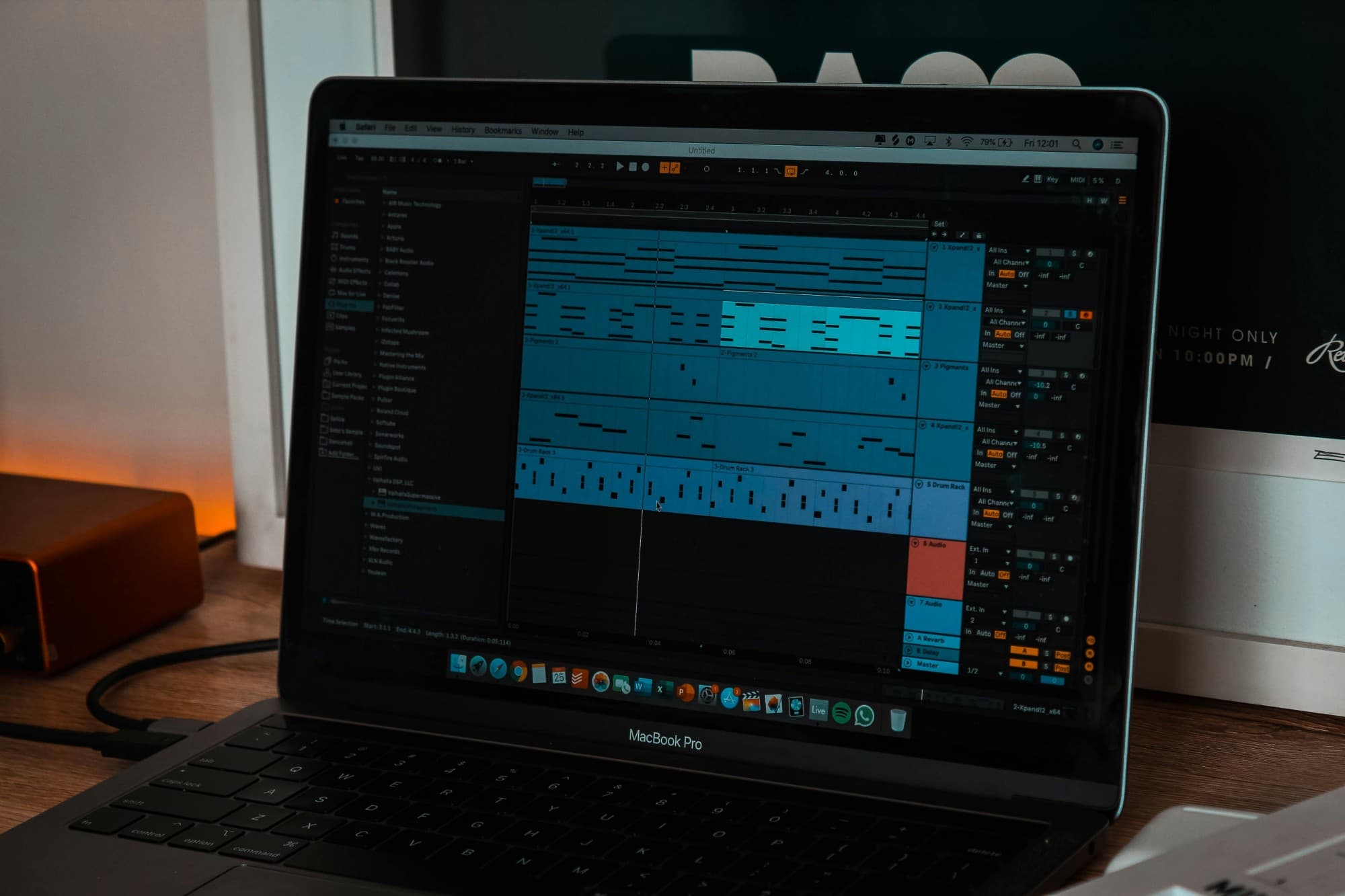 MacBook Pro on a wooden desk running a DAW, warm lamp light to the left